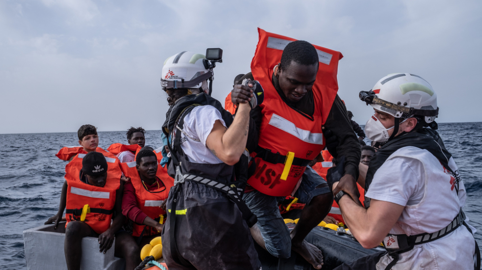 Zwei Mitarbeiter*innen von Ärzte ohne Grenzen helfen einem Mann von einem Holzboot auf das Deck eines Schiffes