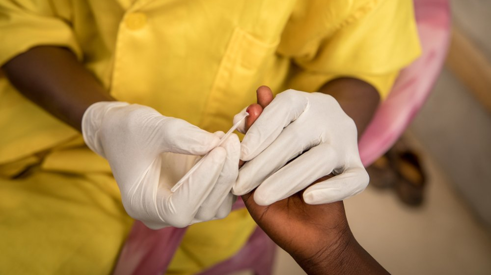 Hände von medizinischem Personal die eine Blutprobe aus einem Finger nehmen