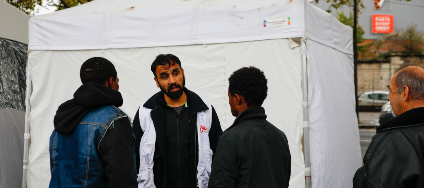 Migranten und ein Mitarbeiter vor einer mobilen Klinik in Calais