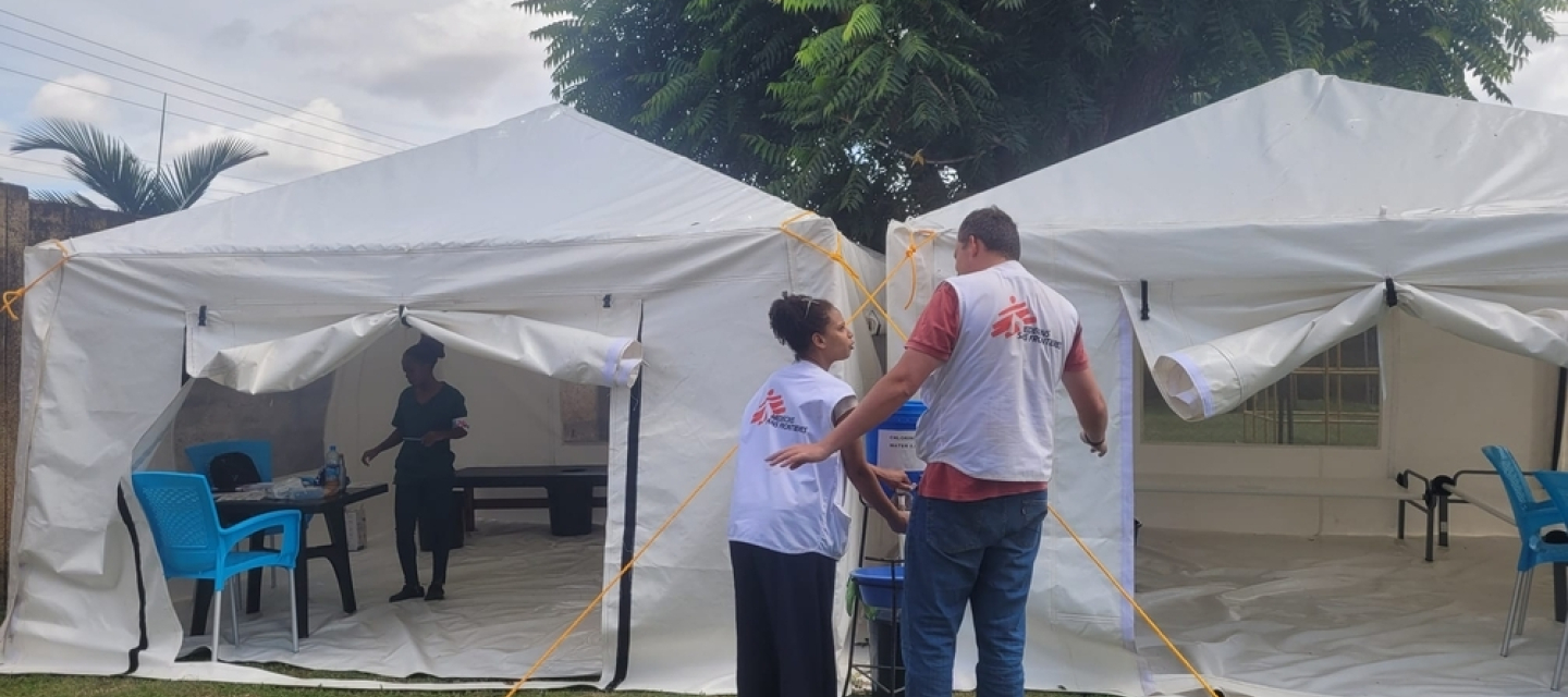 Zwei Mitarbeitende vor einem Zelt, in dem Cholera behandelt wird.