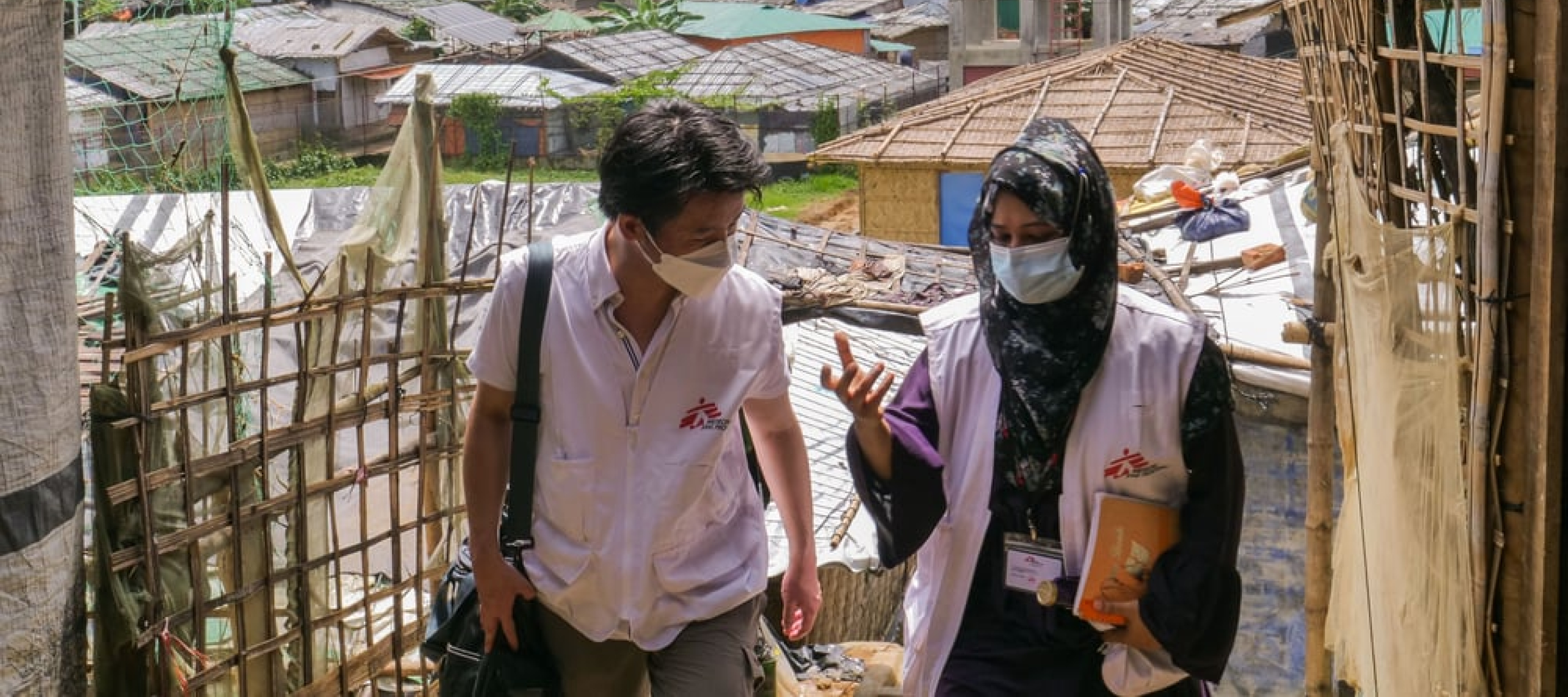 Zwei Personen mit Ärzte ohne Grenzen Weste, im Hintergrund ein Camp