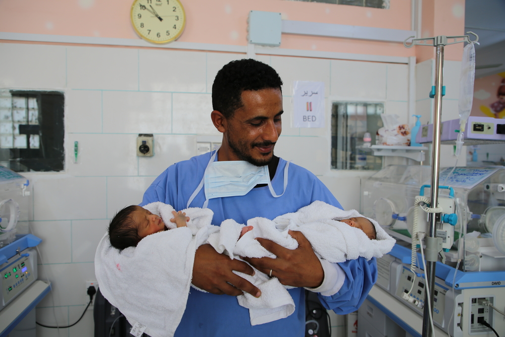 Ein Vater hält seine neugeborenen Zwillinge im Arm 