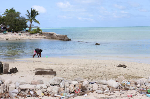 Eine Person am Strand vor einem gebrochenen Deich auf Kiribati