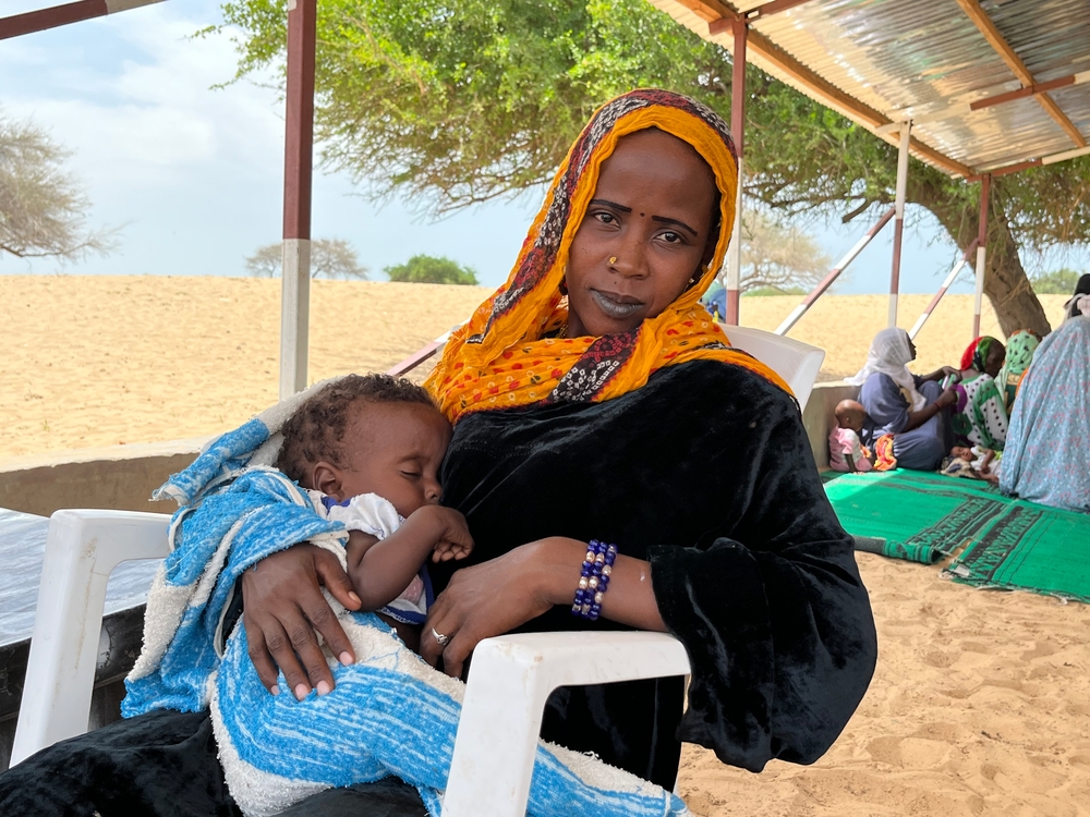 Frau sitzt mit Kind auf dem Arm in Plastikstuhl