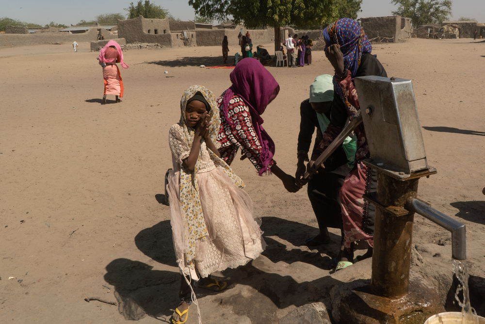 Vier Frauen stehen um eine Wasserquelle.