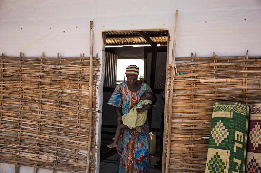 Frau mit Kleinkind im Arm kommt aus Tür