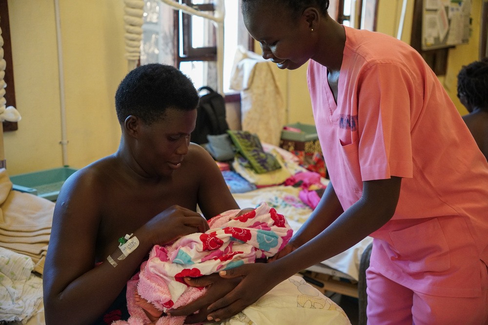 Mitarbeitende an Bett von Frau mit Baby in Arm leitet Haltung an