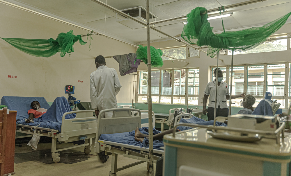 Fotografie eines Zimmers im Homa Bay Hospital; zwei Ärzt*innen machen Visite bei den Patient*innen