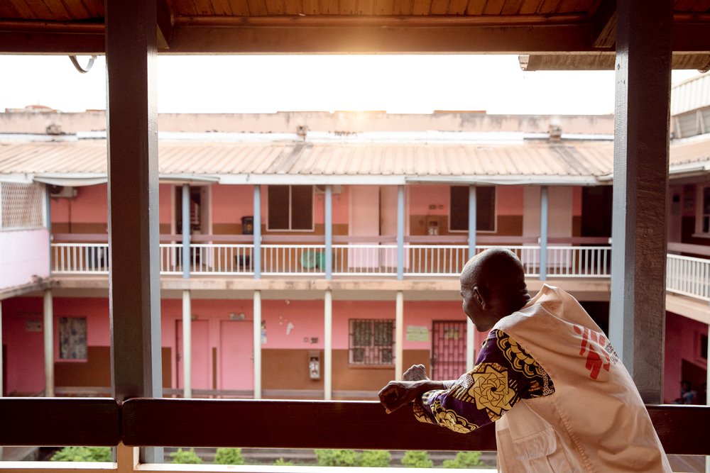 Ein Sozialarbeiter mit einem Ärzte ohne Grenzen Kittel schaut in den Hinterhof eines Hauses, wendet der Kamera den Rücken zu