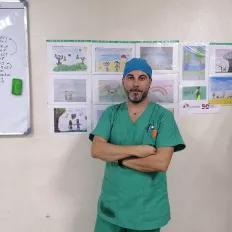 Davide Musardo vor einer Wand mit Kinderbildern in OP-Kleidung