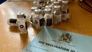 Auf einem Tisch stehen HPV Impfdosen und ein Impfzertifikat.