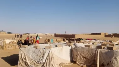 Menschen stehen in der Wüste Nigers auf einer offenen Fläche mit provisorischer Behausung.