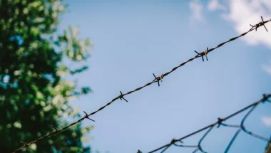Ein Zaun mit Stacheldraht vor blauem Himmel