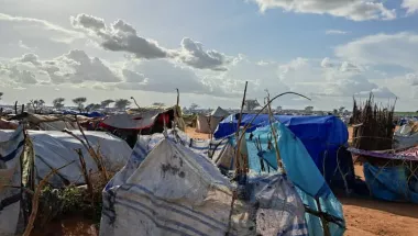 Plastikplanen sind auf Stöckern im Kreis gespannt, dahinter Zelte