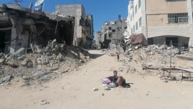 Junge sitzt auf Sandstraße in zerstörter Stadt