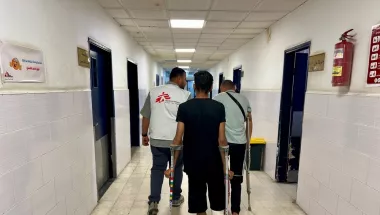 Mitarbeitende und Patient auf Krücken in Krankenhausgang