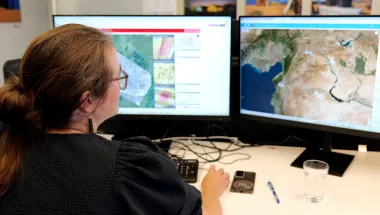Ann De Schutter sitzt vor Monitoren, die Karten zeigen.