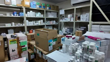 Lagerraum einer Klinik-Apotheke mit Regalen voller Medikamentenschachteln und Kartons sowie Arbeitsfläche mit Arzneiflaschen.