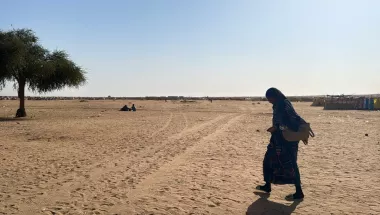 Eine Frau geht alleine über eine freie sandige Fläche.