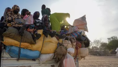 Mehrere Menschen sitzen dicht gedrängt auf einem überladenen Transporter.