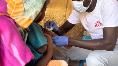 Mitarbeiter impft ein Kind welches im Arm der Mutter liegt