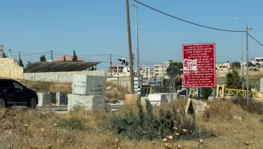 Mehrere Betonblöcke versperren eine Straße neben einem roten Warnschild; im Hintergrund stehen Häuser.