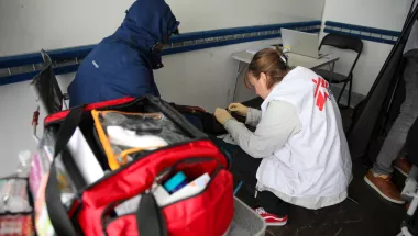 Eine Mitarbeiterin von Ärzte ohne Grenzen versorgt mit Handschuhen das Knie einer sitzenden Person, während im Vordergrund eine geöffnete rote Notfalltasche steht.