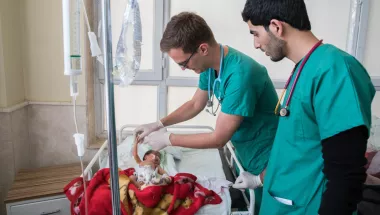 Zwei Mitarbeiter kümmern sich um ein Neugeborenes in einem Bett