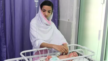 Krankenpflegerin behandelt Neugeborenes in Kinderbett