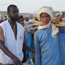 Ein junger Mann mit Material für eine Notunterkunft und ein Mitarbeiter von Ärzte ohne Grenzen in Mali.