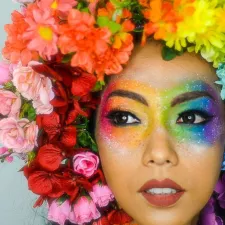 Frau mit regenbogenfarbenem Blumenkranz und Augenmakeup.
