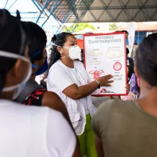 Venezolanische Migrant*innen und Geflüchtete in Nordbrasilien Eine Frau mit Maske spricht vor Anderen, ein Plakat zu Kontrazeptiva in der Hand