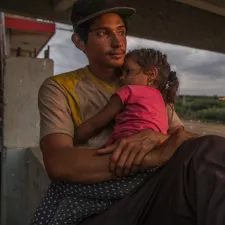 Foto eines jungen Mannes, der seine Tochter im Arm hält Flucht: junger Mann mit Tochter auf Arm