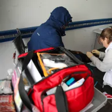 Mitarbeitende beugt sich über Beine von sitzender Person 