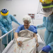 Alte Frau wird von zwei Pflegern in Schutzkleidung betreut