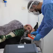 Ein Mann in blauem Schutzanzug beugt sich zu einem Mann herunter, der künstlich beatmet wird