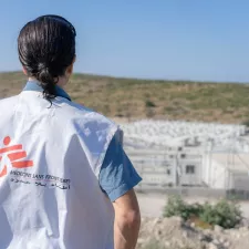 Eine Person von hinten fotografiert, mit einer Ärzte ohne Grenzen Weste die auf ein entferntes Camp schaut