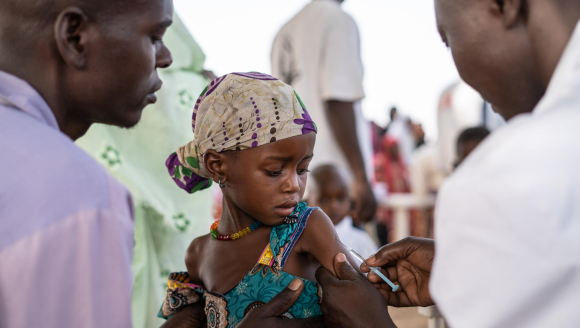 A man supports a small child, while a health care worker gives her a vaccination.