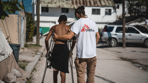 Ein Mitarbeiter von Ärzte ohne Grenzen stützt einen Mann auf Krücken
