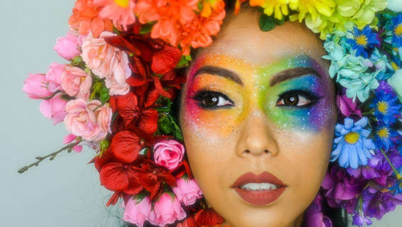 Frau mit regenbogenfarbenem Blumenkranz und Augenmakeup.