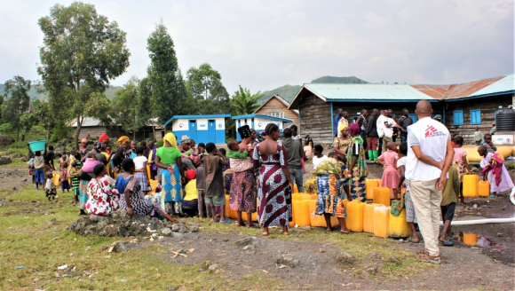 Die Bewohner*innen der Geflüchtetenunterkunft warten darauf, ihre Kanister mit Trinkwasser zu füllen 