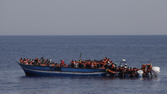 232 in Seenot geratene Menschen mit Rettungswesten auf einem Holzboot im Mittelmeer