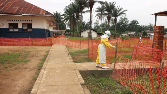 Person in Schutzanzug vor Zaun vor einem Ebolabehandlungszentrum in der DR Kongo.