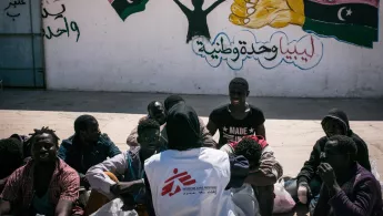 Eine Gruppe von Menschen sitzt auf dem Boden vor einem Gebäude