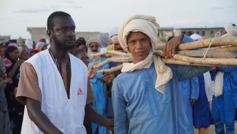 Ein junger Mann mit Material für eine Notunterkunft und ein Mitarbeiter von Ärzte ohne Grenzen in Mali.
