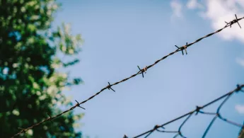 Ein Zaun mit Stacheldraht vor blauem Himmel
