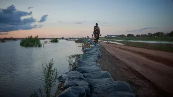 Frau läuft im Südsudan einen Deich enlang - Flutwasser ist überall.