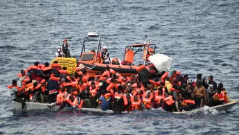 Ein Schlauchboot liegt neben einem massiv überfüllten Holzboot