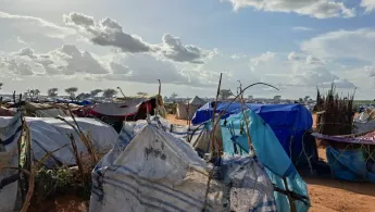 Plastikplanen sind auf Stöckern im Kreis gespannt, dahinter Zelte