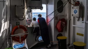 Zwei Jungen stehen am Fenster eines Schiffes und schauen auf das Meer.
